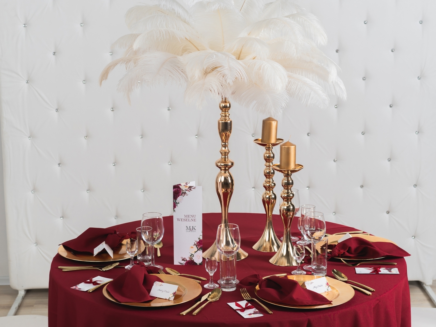 Okrągły stół weselny nakryty bordowym obrusem premium, złota zastawa i ciemne kwiaty w stylu Moody Wedding – oferta wynajmu tekstyliów eventowych