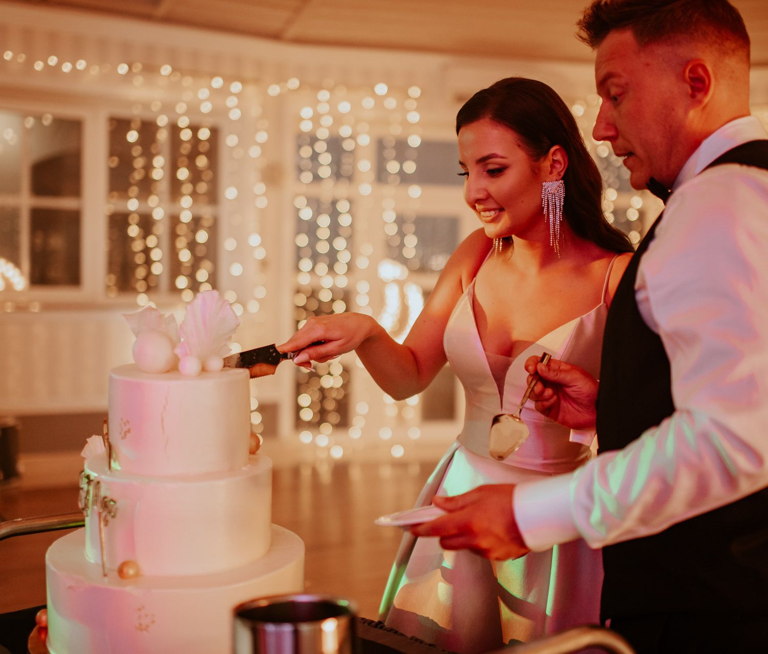 tort weselny krojenie tortu najlepszy tort na wesele girlandy żarówkowe wesele i ślub wynajem dekoracji wynajem artykułów dekoracyjnych Fot: Imagine Weddings