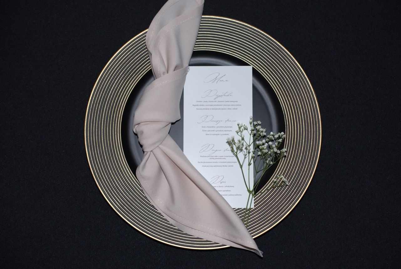 Wynajem podtalerzy w kolorze czarnym z dodatkami złota - idealne dekoracje stołu na wesele i event. Podtalerze czarne z złotymi detalami, pasujące do stylów dekoracyjnych: nowoczesnego, glamour, minimalistycznego i klasycznego. Można je łączyć z dodatkami w odcieniach białego, srebrnego, czerwieni lub różowego, tworząc elegancką i efektowną aranżację stołu.