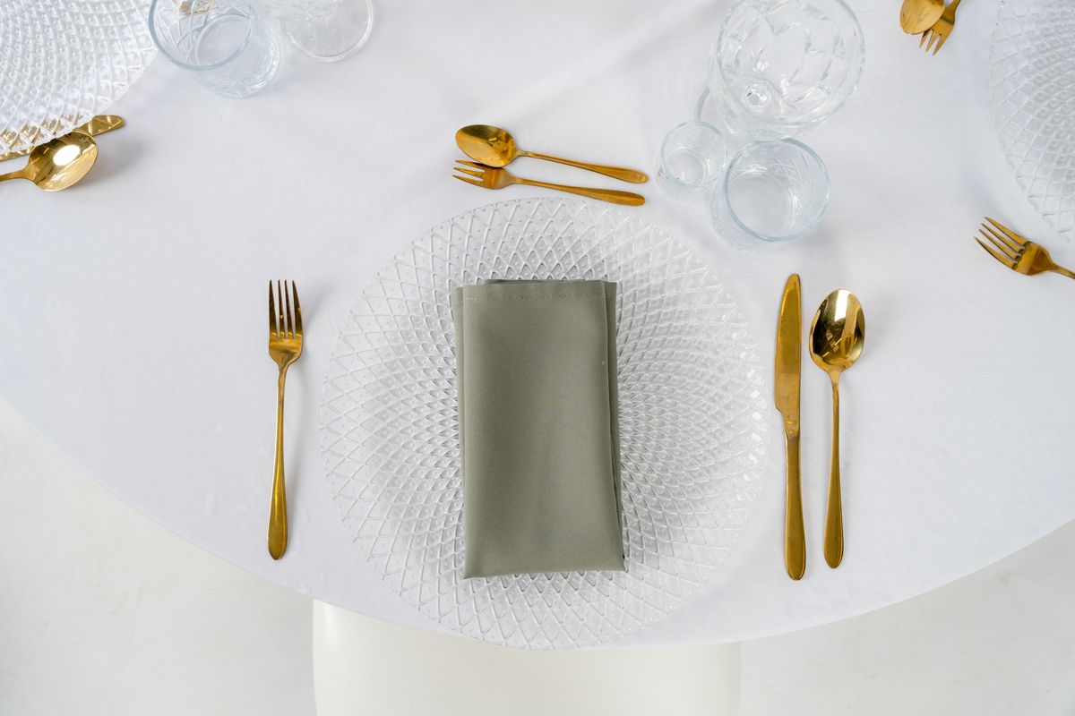 Serwetka oliwkowa na weselu w stylu modern organic – dekoracja stołu z porcelaną, złotymi sztućcami i zielonymi tekstyliami eventowymi.