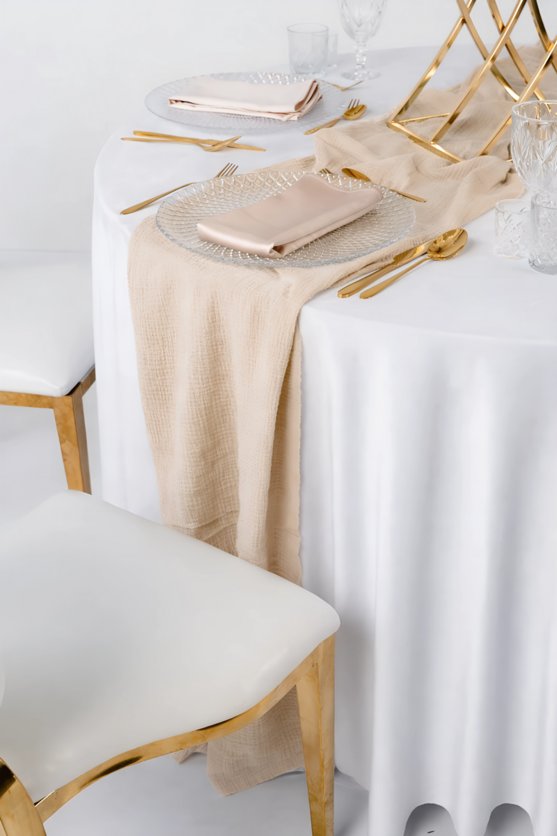 Beżowy bieżnik muślinowy o gniecionej strukturze, luźno udrapowany na ciemnym drewnianym stole – naturalna dekoracja weselna w stylu Boho i Modern Rustic, wynajem tekstyliów