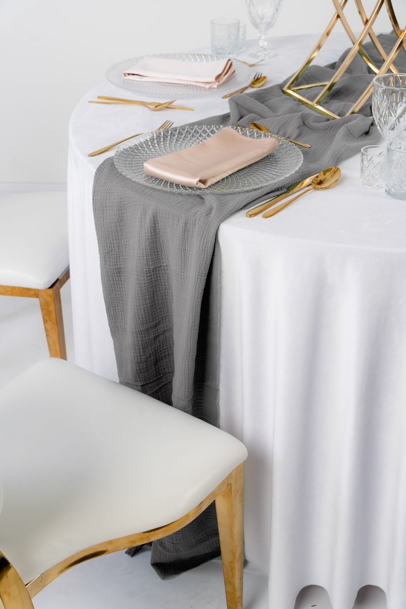 Bieżnik muślinowy w kolorze gołąbkowym (jasnoszary) ułożony w miękkie fale na drewnianym stole – minimalistyczna dekoracja weselna w stylu Scandi i Loft, wynajem tekstyliów eventowych