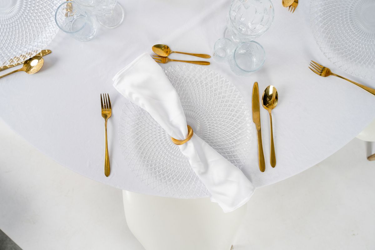 Detal nakrycia stołu: złota spiralna obrączka na materiałowej serwetce – nowoczesna biżuteria stołowa na wesele w stylu Modern Glamour