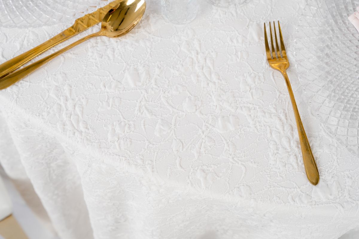 Detal białego obrusu żakardowego o wypukłej strukturze – luksusowa tkanina eventowa z geometrycznym wzorem, matowy splot premium na wynajem