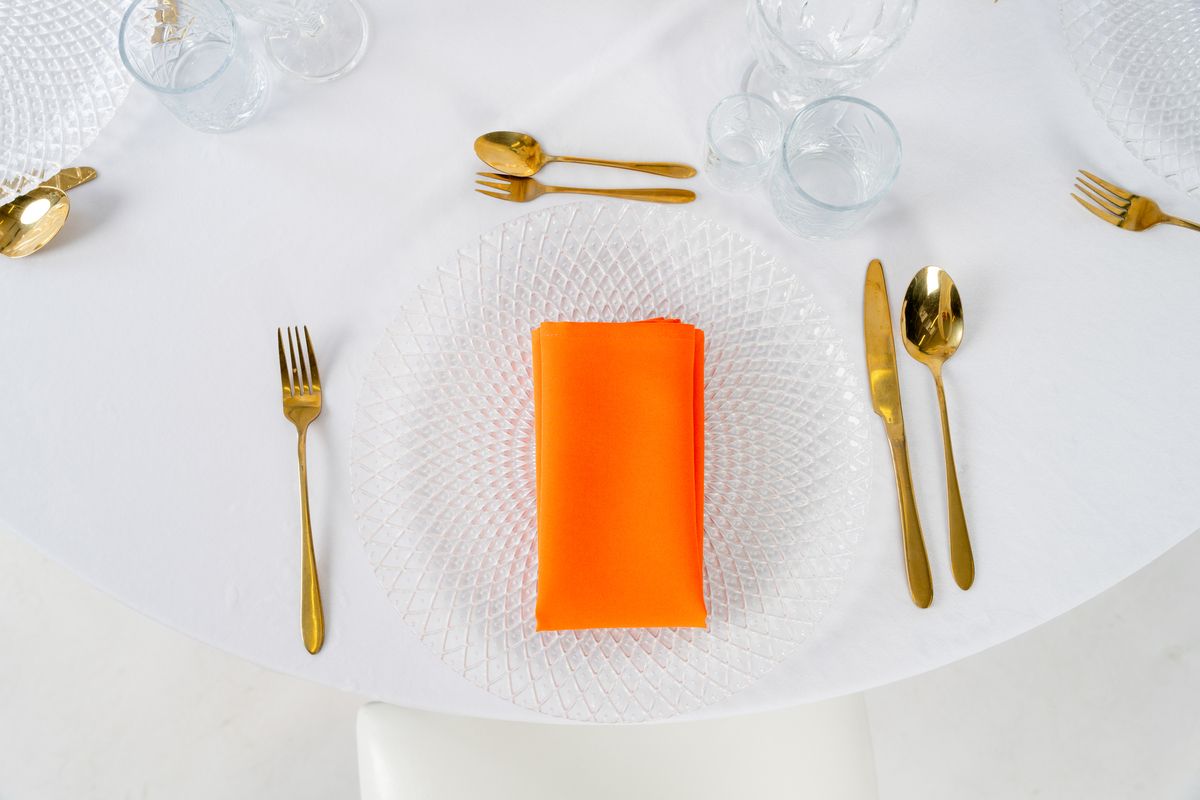 Serwetka materiałowa pomarańczowa w aranżacji boho – dekoracja stołu weselnego ze złotymi sztućcami i talerzem z kamionki.