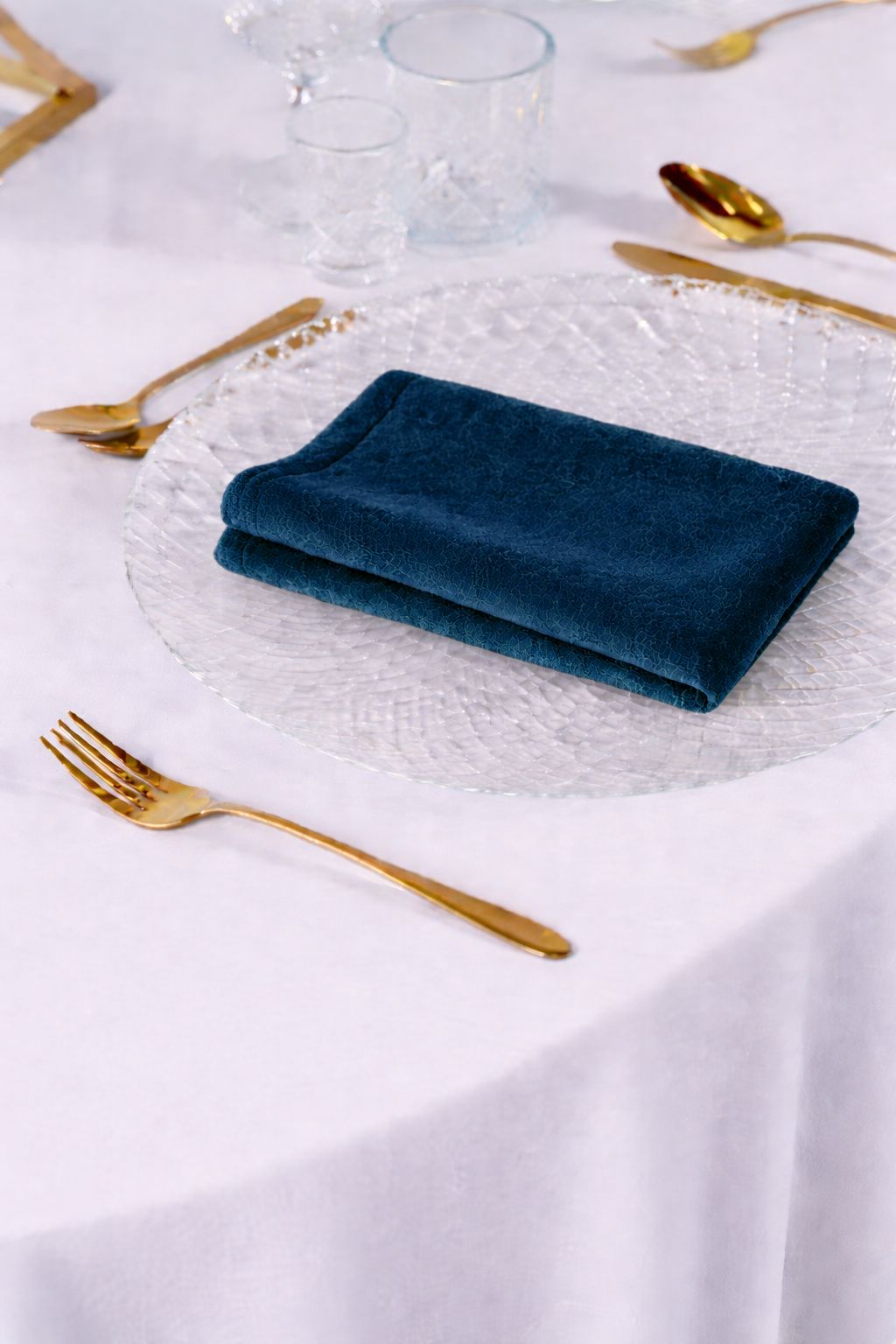 Elegancka aranżacja stołu weselnego z granatowymi serwetkami welurowymi, złotymi sztućcami i białą porcelaną – styl Royal Glamour, wypożyczalnia tekstyliów eventowych