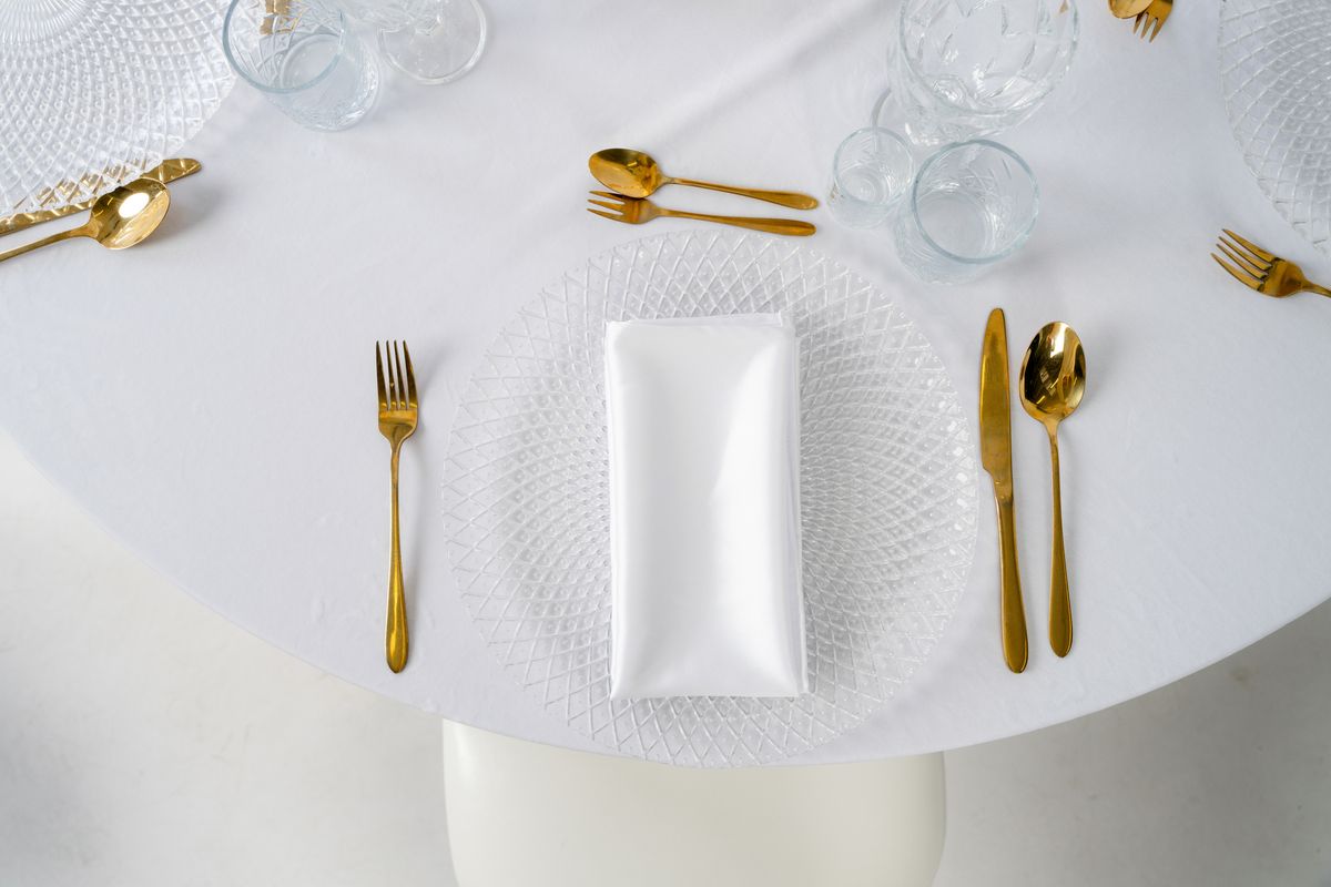 Białe serwetki satynowe na wynajem ułożone na złotej zastawie – elegancka dekoracja stołu weselnego w stylu Classic Glamour, wypożyczalnia tekstyliów.