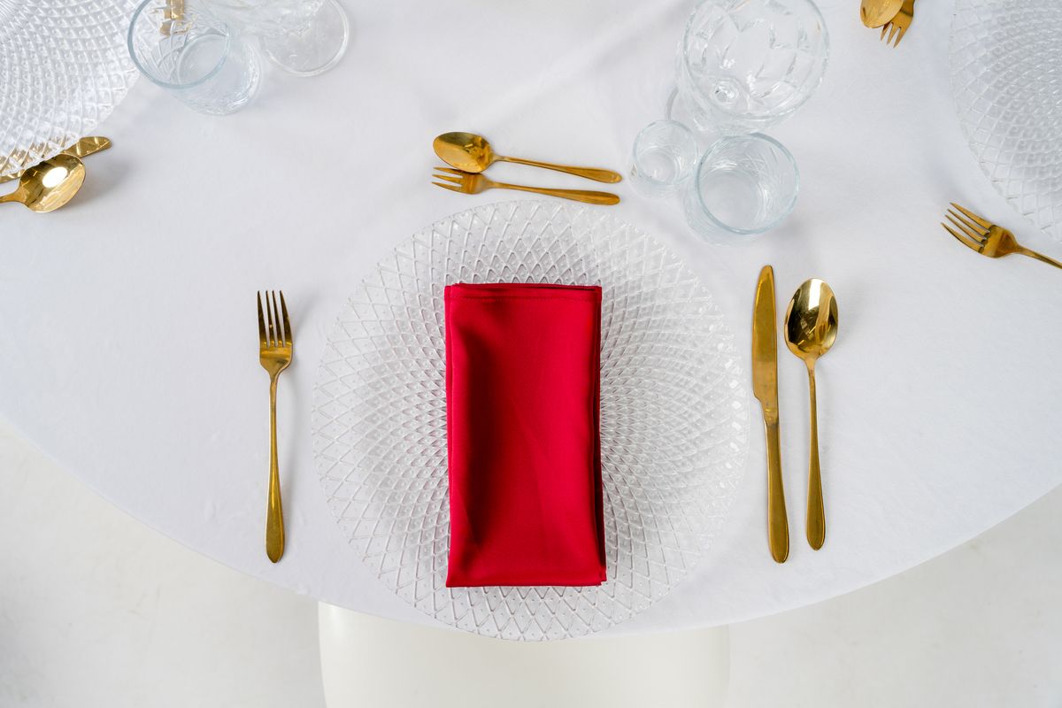 Bordowe serwetki satynowe na wynajem, ułożone na złotych podtalerzach – elegancka dekoracja stołu weselnego w stylu Burgundy Glamour.