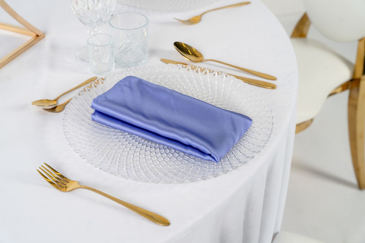 Serwetka satynowa granatowa złożona w elegancką formę na białym talerzu – dekoracja stołu weselnego w stylu glamour, wypożyczalnia tekstyliów.