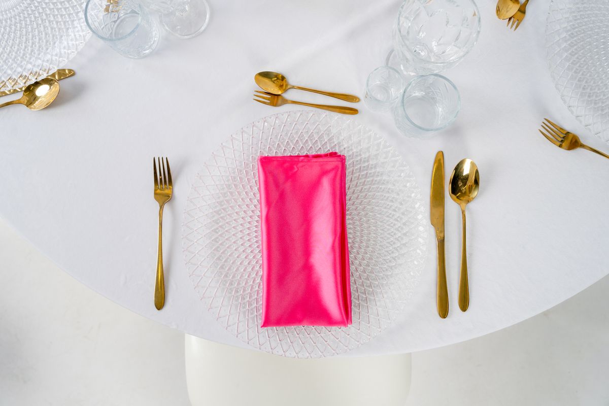 Różowe serwetki satynowe na złotych podtalerzach z kwiatową dekoracją – eleganckie nakrycie stołu weselnego w stylu Romantic Glamour, wypożyczalnia dekoracji.