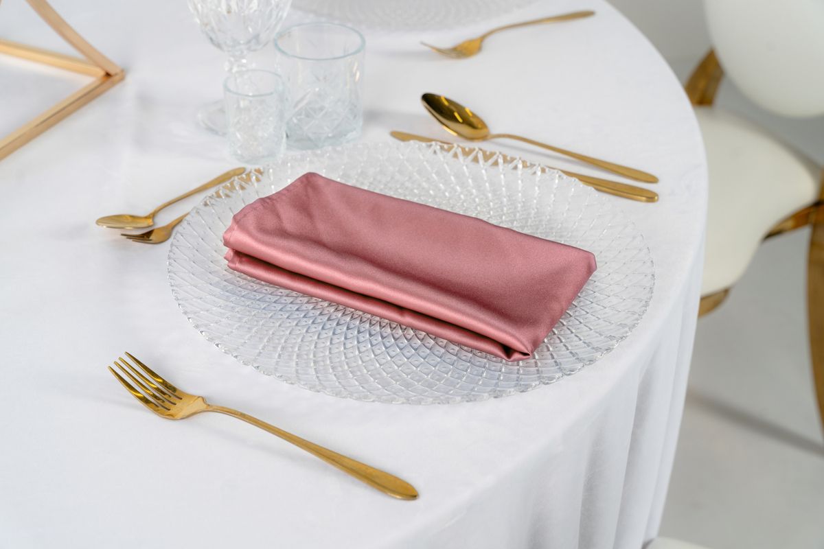 Różowe serwetki satynowe na złotych podtalerzach z kwiatową dekoracją – eleganckie nakrycie stołu weselnego w stylu Romantic Glamour, wypożyczalnia dekoracji.